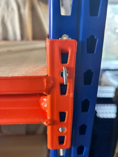 An orange beam connector with a safety pin, hooked into a blue upright.